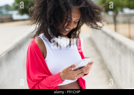 Eine junge Mischenrennen Frau anhören von Musik auf einem Smartphone mit Kopfhörern im freien Stockfoto