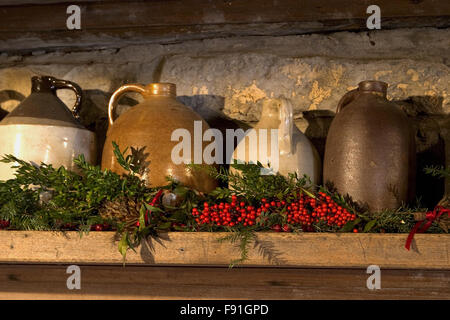 Crock Krüge auf Kaminsims mit Weihnachtsschmuck und Beeren in einer Blockhütte am Museum von den Appalachen, Tennessee, USA. Stockfoto