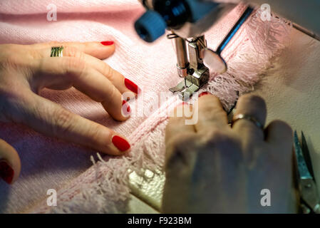 In der Nähe von weiblichen Händen mit lackierten Fingernägeln Fringe Kante stricken rosa Kleid nähen und beleuchtet durch Licht auf Nähen Ma Stockfoto