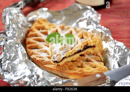 Scheiben des Gitters gekrönt Konfitüre Torte auf einer Alufolie Stockfoto