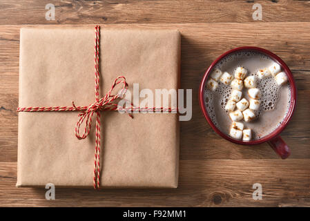 Vogelperspektive Blick auf eine braune Normalpapier eingewickelt neben eine große Tasse heißen Kakao mit Marshmallows Christmas Present. Stockfoto