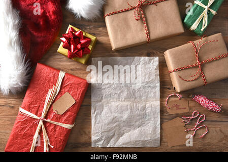 Draufsicht des umschlossenen Weihnachten präsentiert auf einem rustikalen Holztisch mit String, Geschenkanhänger und Weihnachtsmütze. Querformat mit Stockfoto