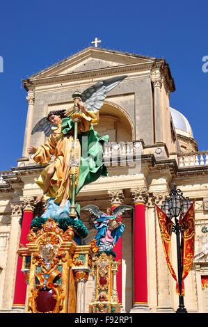 farbenfrohe Statue geflügelte Dame auf einem Sockel vor der Dorfkirche in Malta, im Sommer. Stockfoto