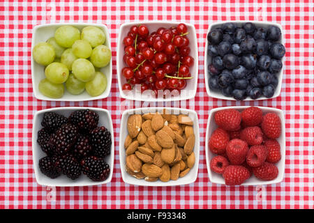 Rote Johannisbeeren, Weintrauben, Brombeeren, Mandeln, Himbeeren und Heidelbeeren in weißen Schalen auf einem aufgegebenen Hintergrund. Stockfoto