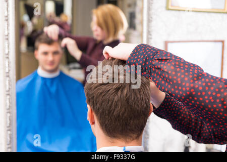 Rückansicht des jungen Mann die Haare geschnitten und gestylt von Stylistin im Salon mit von Fokus Reflexion im Hintergrund Spiegel hautnah Stockfoto