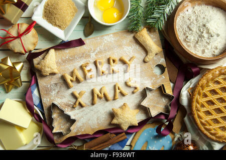 Weihnachten Hintergrund mit merry Xmas Backen gemacht von Cookies auf ein Schneidebrett, umgeben von Kuchen und Zutaten Stockfoto