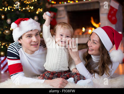 Glückliche Familie mit Kind Sohn liegen in der Nähe von Weihnachtsbaum und Kamin im Wohnzimmer Stockfoto