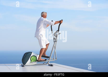 gesunde Senioren Mann arbeiten auf Fitness Laufband Maschine im modernen Haus Terrasse mit Meerblick Stockfoto