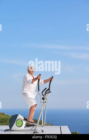 gesunde Senioren Mann arbeiten auf Fitness Laufband Maschine im modernen Haus Terrasse mit Meerblick Stockfoto