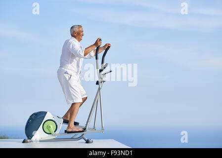 gesunde Senioren Mann arbeiten auf Fitness Laufband Maschine im modernen Haus Terrasse mit Meerblick Stockfoto