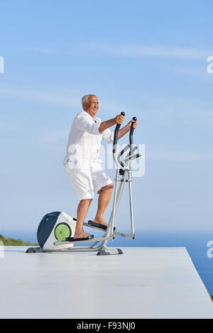 gesunde Senioren Mann arbeiten auf Fitness Laufband Maschine im modernen Haus Terrasse mit Meerblick Stockfoto