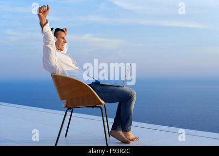 hübscher junger Mann, entspannen und arbeiten auf Laptop-Computer zu Hause Balkon während aussehende Sonnenuntergang Stockfoto