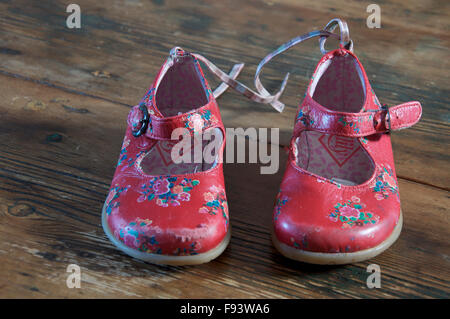 Ein gut getragen paar kleine Mädchen helle rote Schuhe auf einem alten Holzboden gelegt. Stockfoto