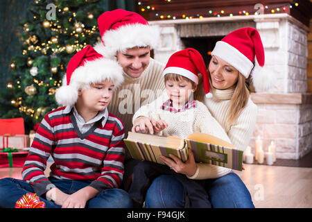 Familie, die Überprüfung der Fotos im Album zusammen in der Nähe von Weihnachtsbaum vor Kamin Stockfoto