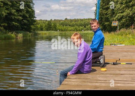 Spychowo, Polen - 23. Juli 2015: Jungen sitzen auf einer Holzbrücke und Angeln. Stockfoto