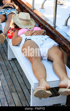 Kykladen, Santorin, Thira. Junge Frau im Bikini, Festlegung auf der Werkbank an Deck Exkursion Boot, schlafend, mit Strohhut für Gesicht. Stockfoto