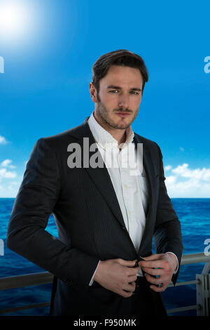 Schönen jungen Mann gelehnt Handlauf auf Kreuzfahrtschiff, tragen Business-Anzug, Blick in die Kamera Stockfoto