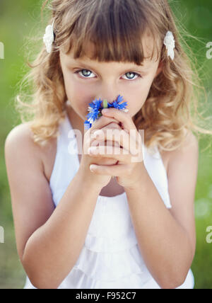 Niedliche kleine Mädchen mit Blumen spielt im Frühlingspark. Stockfoto