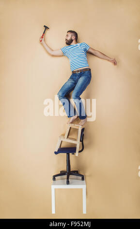 Handwerker, die gefährlich auf einen Haufen von Stühlen stehend. Studio auf einem beigen Hintergrund gedreht. Stockfoto