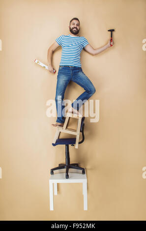 Handwerker, die gefährlich auf einen Haufen von Stühlen stehend. Studio auf einem beigen Hintergrund gedreht. Stockfoto