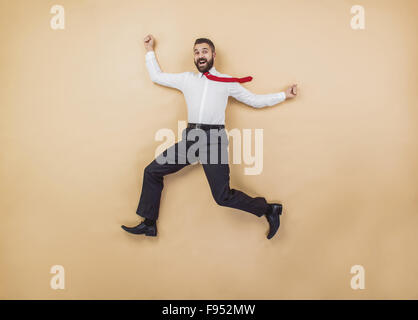 Glücklich-Manager in einer siegreichen Pose hoch springen. Studio auf einem beigen Hintergrund gedreht. Stockfoto