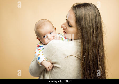 Mutter mit einem Baby zärtlich in ihr Arme Studio gedreht auf Beige Hintergrund Stockfoto