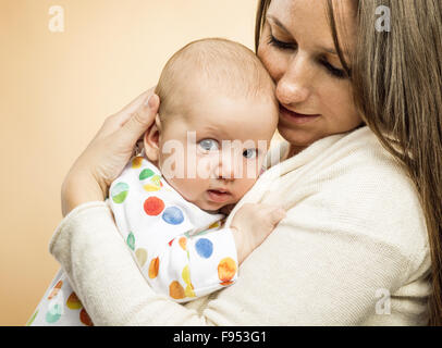 Mutter mit einem Baby zärtlich in ihr Arme Studio gedreht auf Beige Hintergrund Stockfoto