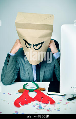 ein junger kaukasischer Geschäftsmann mit einem Papier Tasche in seinem Kopf mit einem traurigen Gesicht sitzt an seinem Schreibtisch, mit einem Rentier-Geweih er Stockfoto