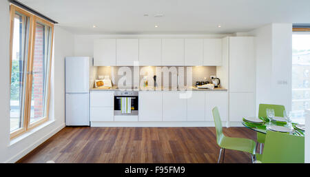 Ein Church Square, London, UK. Innenansicht der eine offene Küche und Wohnzimmer Fläche. Weiße Küchenzeile mit Holzböden. Moderne Architektur und Möbel. Großen Fenstern, die geöffnet zu kippen. Stockfoto