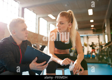 Schuss von personal Trainer und junge Frau diskutieren Fitnessplan. Personaltrainer zeigen etwas auf Zwischenablage Schüler ich Stockfoto