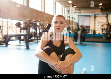 Porträt einer jungen Frau im Fitness-Studio, eine Pause von Training. Kaukasische Weibchen sitzt entspannt am Boden und Blick in die Kamera. Stockfoto
