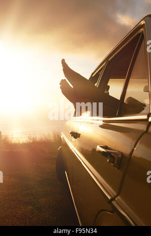 Sommer Urlaub Offroad Reise-Konzept. Frau, hängen ihre Beine aus Autofenster bei Sonnenuntergang. Stockfoto