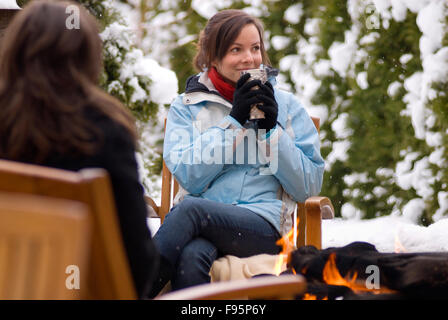 Ein junges Mädchen genießt ein heißes Getränk im Winterschnee von einem Outdoor-Feuer. Stockfoto