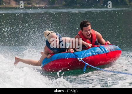 Brett und Kali lachen, als sie an das Rohr festhalten auf wie es hinter dem Boot, am Kalamalka Lake, BC gezogen wird Stockfoto