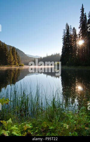 Die Spätsommer-Sonne steigt über Blitz See in Manning Park, BC und bietet eine spektakuläre Reflexion. Stockfoto