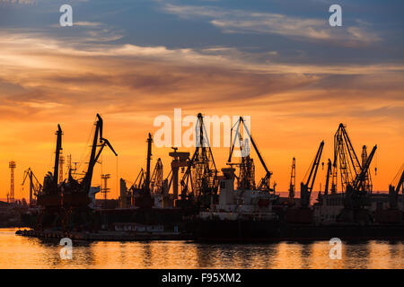 Schwarze Silhouetten von Kränen und Frachtschiffe in Varna Hafen bei Sonnenuntergang unter bunten Himmel Stockfoto