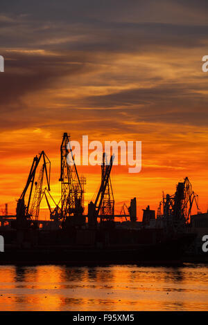 Silhouetten von Kränen und Frachtschiffe im Hafen von Varna bei Sonnenuntergang unter bunten Himmel Stockfoto