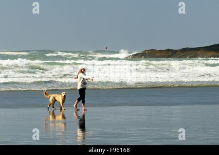 Eine junge Frau und ihr Hund (Golden Retriever) spielen mit einem Ball auf Chesterman Beach in der Nähe von Tofino, BC. Stockfoto