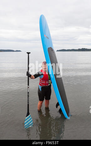 Eine ältere Frau kommt an Land mit ihren Stand-up Paddle Board nach dem Paddeln in den Gewässern von Geschichten Strand in der Nähe von Port Hardy Stockfoto