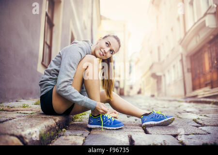 Junge weibliche Läufer ist ihre Laufschuhe auf gefliesten Bürgersteig im alten Stadtzentrum binden. Stockfoto