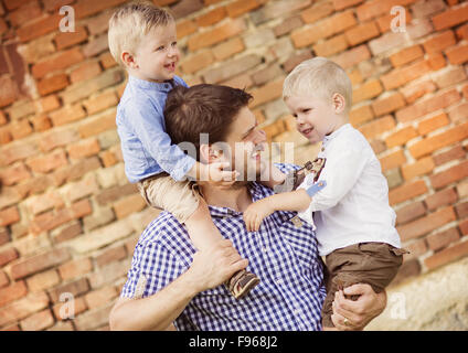 Glückliche junge Vater mit seinen beiden kleinen Söhnen gemeinsam Spaß haben in der Natur durch das alte Backsteinhaus Stockfoto