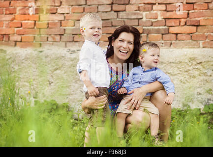 Glückliche junge Mutter mit ihren zwei kleinen Söhnen gemeinsam Spaß haben in der Natur durch das alte Backsteinhaus Stockfoto