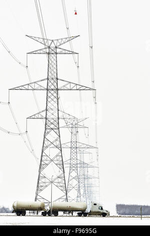 Eine Zugmaschine Anhänger unterquert Transmittiom Stromleitungen, die überqueren der Landstraße in Alberta Kanada zeigt die Emense Größe Stockfoto