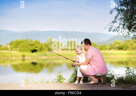 Glückliche junge Vater Angeln auf dem See mit seiner kleinen Tochter Stockfoto