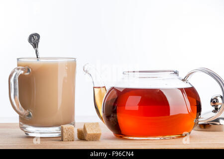 Milch löst sich im Glastasse heißen Tee auf mit Teekanne über weiß Stockfoto