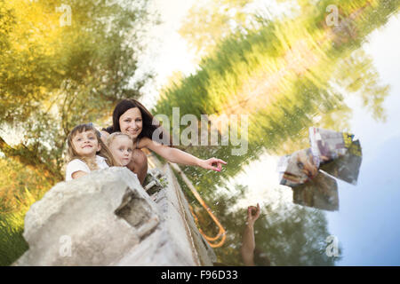 Zwei kleine Schwestern und ihre Mutter spielen mit Papier-Boote auf See Stockfoto