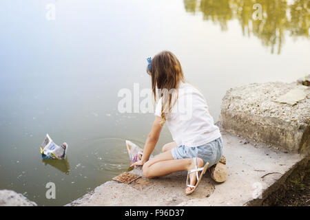 Kleine Mädchen spielen mit Papierschiffchen im Fluss Stockfoto