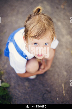 Traurig, kleines Mädchen mit blauen Augen auf der Straße hocken. Stockfoto