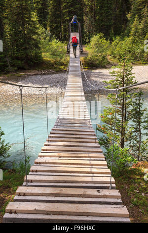 Zwei Rucksacktouristen überqueren eine Hängebrücke eines Flusses in Kootenay National Park, Britisch-Kolumbien, Kanada. -Modell veröffentlicht. Stockfoto