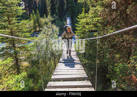 Ein Back Packer kreuzt eine Hängebrücke über einen Fluss in Kootenay National Park, Britisch-Kolumbien Kanada. Model Released Stockfoto